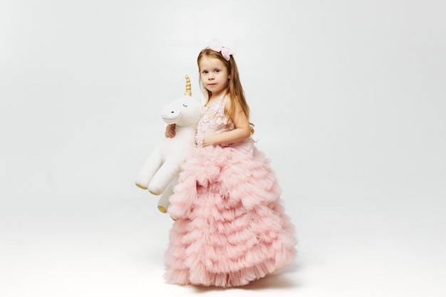 Photo gratuite adorable petite fille mignonne habillée comme une princesse en jupe rose posant isolé et tenant une peluche licorne sous son bras