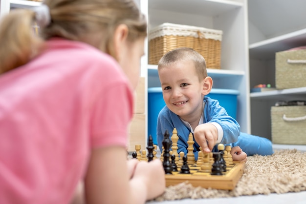 Adorables frères et sœurs allongés sur le sol et jouant aux échecs les uns avec les autres