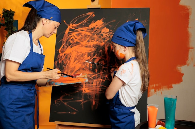 Photo gratuite adulte et enfant utilisant de la peinture orange sur toile