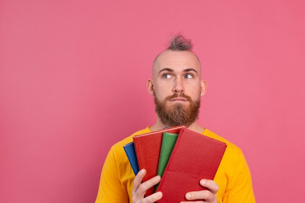 Adulte souriant gars vêtements décontractés avec barbe embrasse les livres préférés à lui-même isolé sur rose