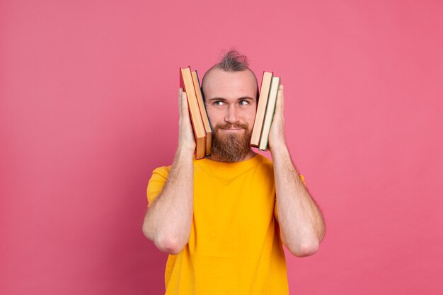 Adulte souriant gars vêtements décontractés avec barbe embrasse les livres préférés à lui-même isolé sur rose