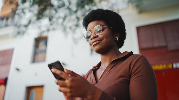 African American curly girl textos avec des amis sur un smartphone