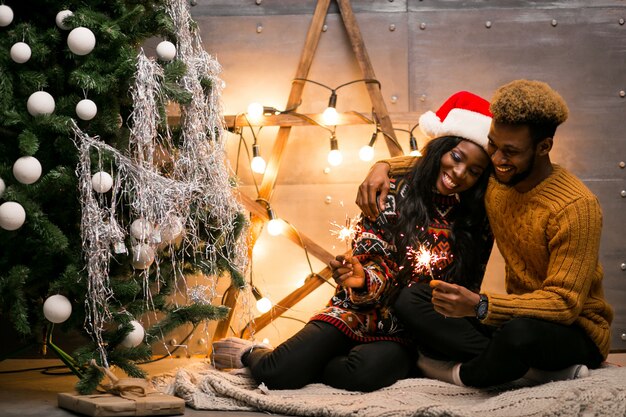 Afro couple américain assis avec des lumières du Bengale par le sapin de Noël