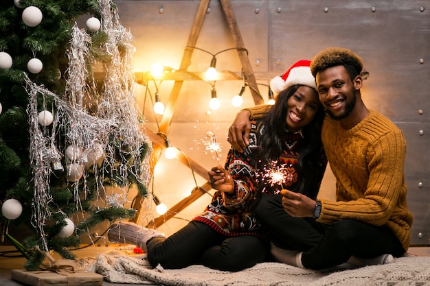 Afro couple américain assis avec des lumières du Bengale par le sapin de Noël