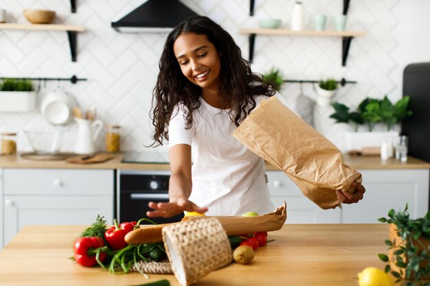 Afro girl publie des produits d'un sac en papier sur la table