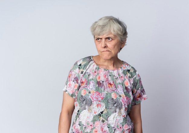 Agacé femme âgée se tient à côté isolé sur mur blanc