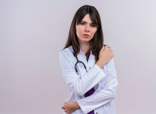 Agacé jeune femme médecin en robe médicale avec stéthoscope met la main sur l'épaule et regarde la caméra sur fond blanc isolé avec copie espace