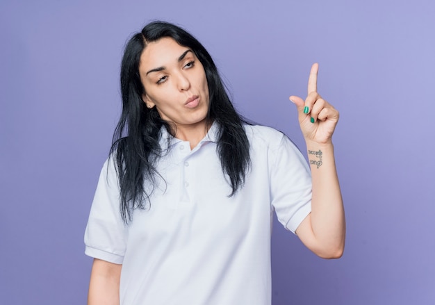 Agacé jeune fille caucasienne brune roule les yeux et pointe vers le haut isolé sur mur violet