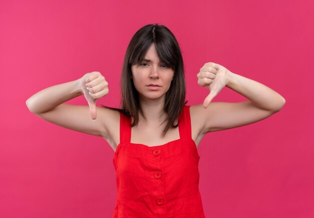 Agacé jeune fille caucasienne pouces vers le bas avec les deux mains et regardant la caméra sur fond rose isolé