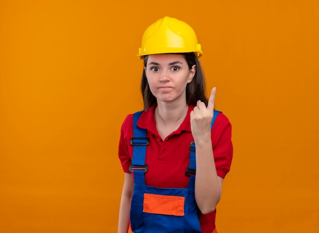 Agacé jeune fille constructeur montre un geste du doigt sur fond orange isolé avec copie espace