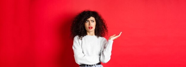 Photo gratuite agacé et perplexe jeune femme aux cheveux bouclés levant les mains et regardant de côté ne comprends pas s