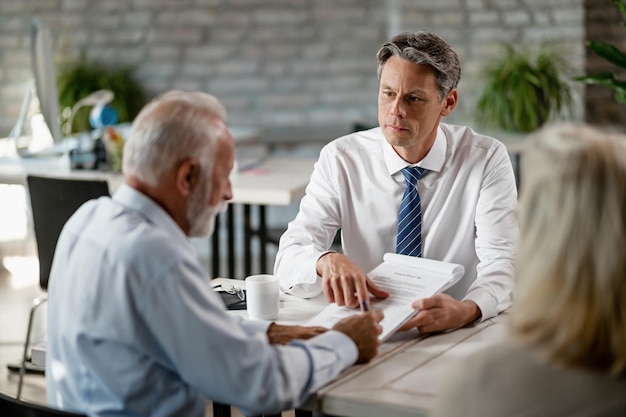 Agent d'assurance ayant une réunion avec des clients seniors et pointant vers le lieu de la signature d'un contrat