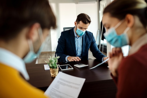 Agent d'assurance avec masque facial calculant les coûts lors d'une réunion avec des clients au bureau