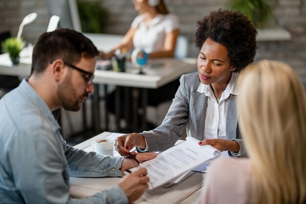 Agent immobilier femme noire montrant à un couple où signer le contrat lors de la réunion au bureau