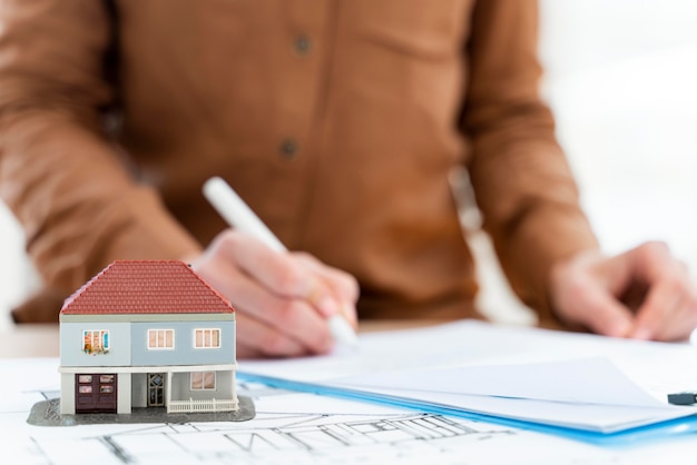 Un agent immobilier signe un contrat sur un bloc-notes à côté d'une maison miniature.