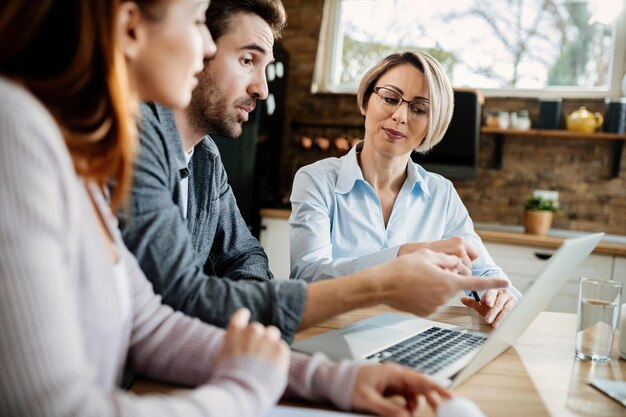 Agent immobilier souriant et jeune couple utilisant un ordinateur portable pendant la réunion