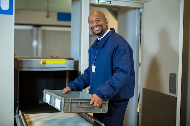 Photo gratuite agent de sécurité de l'aéroport souriant tenant une caisse près de la bande transporteuse