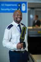 Photo gratuite agent de sécurité de l'aéroport souriant tenant un détecteur de métaux dans le terminal de l'aéroport