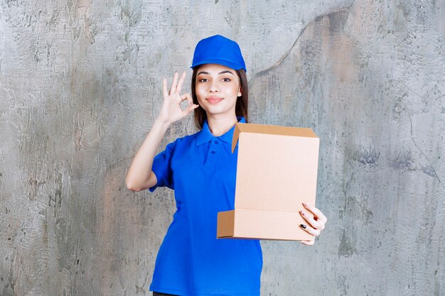 Agent de service féminin en uniforme bleu tenant une boîte en carton ouverte et montrant un signe positif de la main