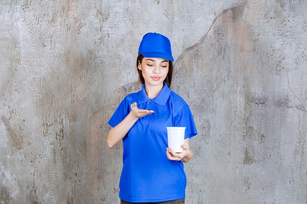 Agent de service féminin en uniforme bleu tenant un gobelet jetable blanc.