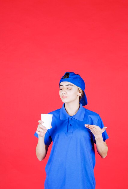 Agent De Service Féminin En Uniforme Bleu Tenant Une Tasse De Boisson Jetable Et Sentant La Saveur.