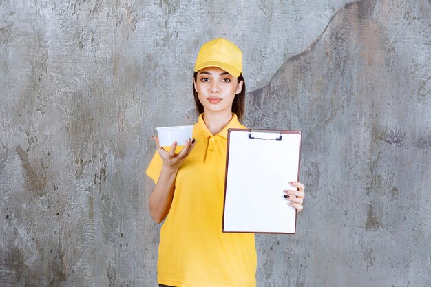 Agent de service féminin en uniforme jaune tenant un bol à emporter en plastique et donnant la liste des clients pour signature.