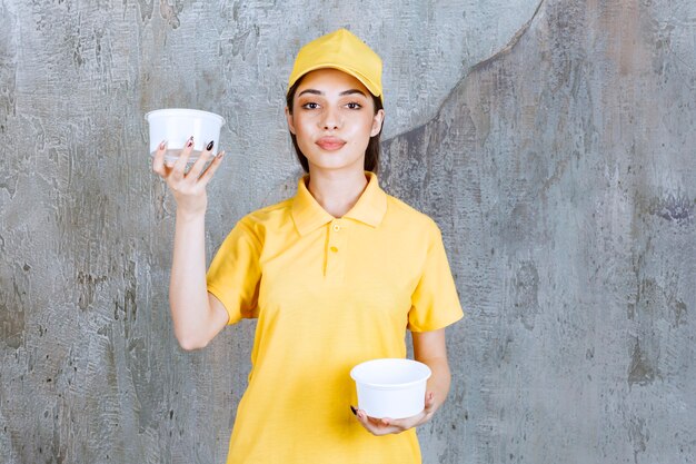 Agent de service féminin en uniforme jaune tenant deux bols à emporter en plastique dans les deux mains