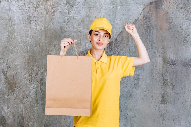 Agent de service féminin en uniforme jaune tenant un sac à provisions et montrant un signe de main positif.