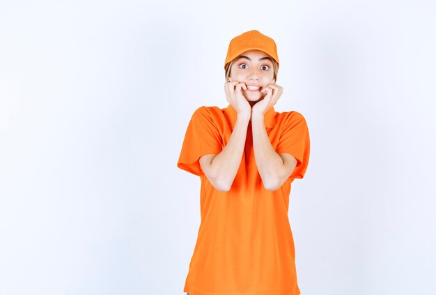 Agent de service féminin en uniforme orange couvrant sa bouche et a l'air effrayé