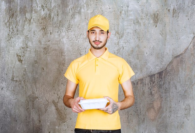 Agent de service masculin en uniforme jaune tenant une boîte à emporter blanche