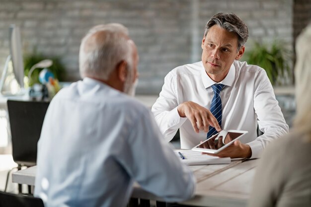 Agents d'assurance utilisant une tablette numérique lors d'une réunion avec des clients seniors au bureau