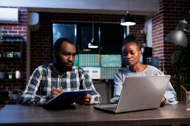 Agents professionnels de la société commerciale assis au bureau tout en examinant les rapports de documentation sur les investissements. Employés d'une agence de fonds spéculatifs assis au bureau dans un espace de travail de bureau tout en analysant des données financières.