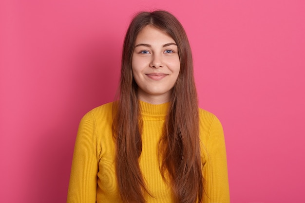 Agréable à la femme de race blanche aux cheveux longs, vêtu d'une chemise décontractée jaune, de bonne humeur, regardant joyeusement la caméra