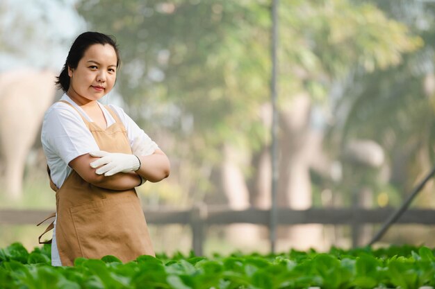 Une agricultrice asiatique aux bras croisés souriant et regardant la caméra tout en se tenant dans le champ de la ferme. Concept de ferme biologique.