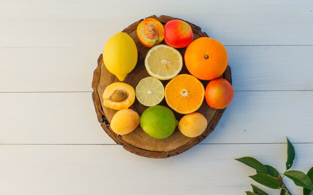 Agrumes avec feuilles, abricots, nectarines sur planche à découper et fond en bois, pose à plat.