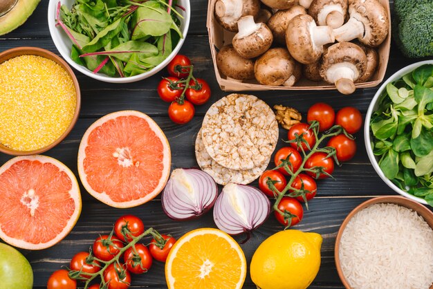 Agrumes; polenta; grains de riz; légumes à feuilles; gâteau de riz soufflé; tomates cerises sur fond en bois