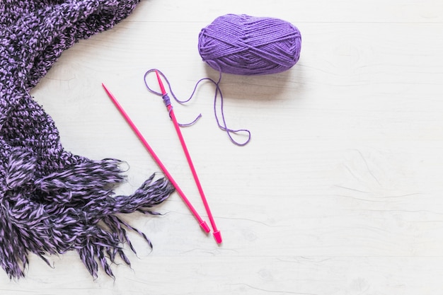 Aiguilles tricotées avec fil violet et écharpe sur fond texturé blanc