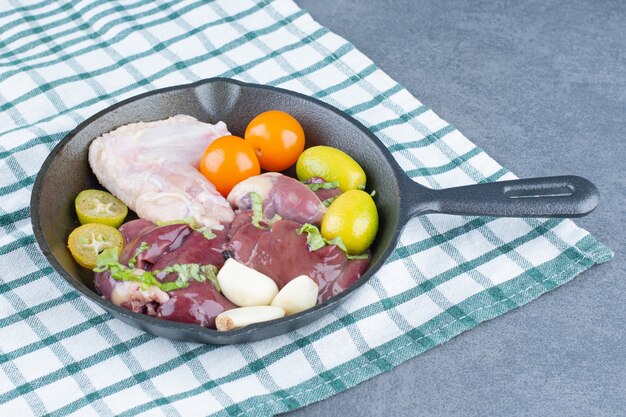 Aile de poulet cru et légumes frais sur une poêle noire.