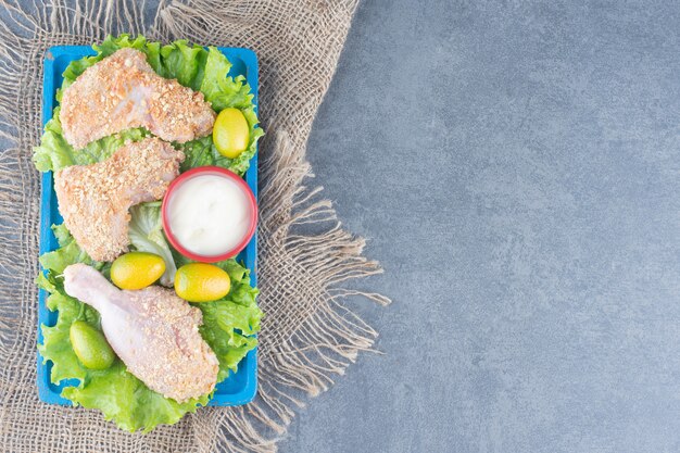 Ailes de poulet avec chapelure et légumes sur plaque bleue.