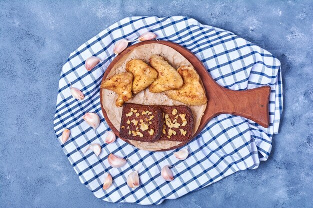 Ailes de poulet frit avec du pain sur une planche de bois sur bleu