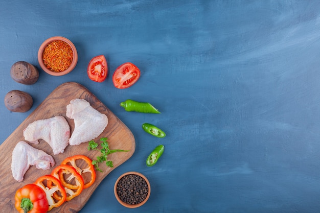 Ailes de poulet et légumes tranchés sur une planche à découper, sur le fond bleu.