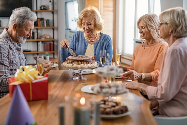 Aînés heureux célébrant l'anniversaire de la femme pendant qu'elle coupe un gâteau à la maison