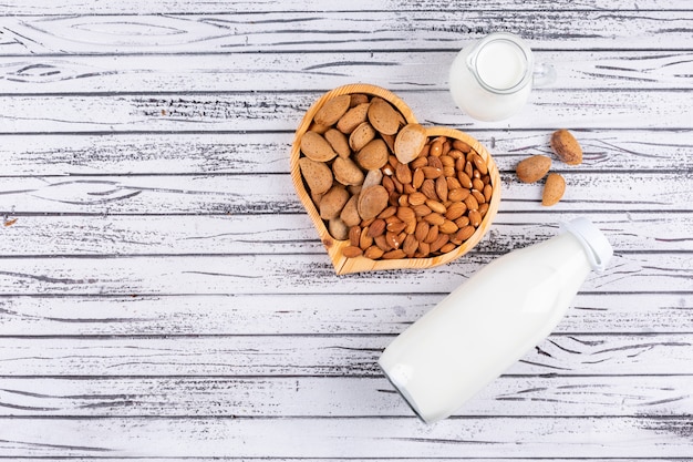 Amande dans une assiette en bois en forme de coeur avec vue de dessus de bouteille de lait sur une table en bois blanc