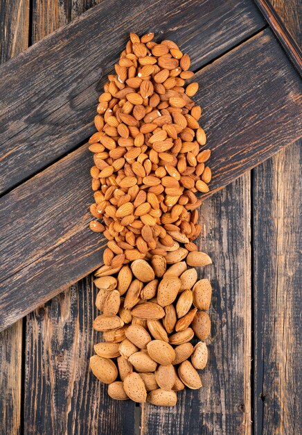 Amandes alignées à plat sur une table en bois foncé. verticale