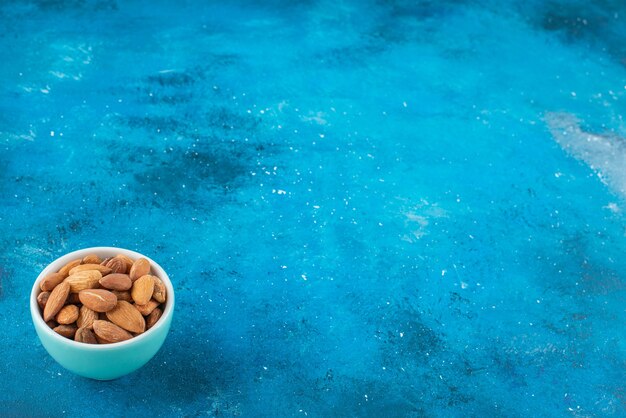 Amandes non décortiquées dans un bol sur la surface bleue