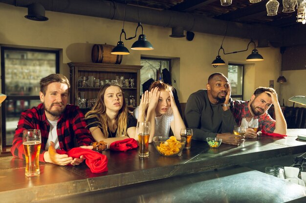 Les amateurs de sport applaudissent au bar, au pub et boivent de la bière pendant le championnat, la compétition se déroule. Groupe multiethnique d'amis excités de regarder la traduction. Émotions humaines, expression, concept de soutien.