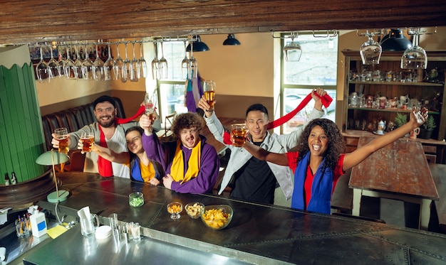 Les amateurs de sport applaudissent au bar, au pub et boivent de la bière pendant le championnat, la compétition se déroule. Groupe multiethnique d'amis excités de regarder la traduction. Émotions humaines, expression, concept de soutien.