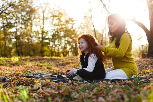 Ambiance d&#39;automne, portrait de famille. Charmante maman et sa fille aux cheveux roux s&#39;amusent assises sur le tombé