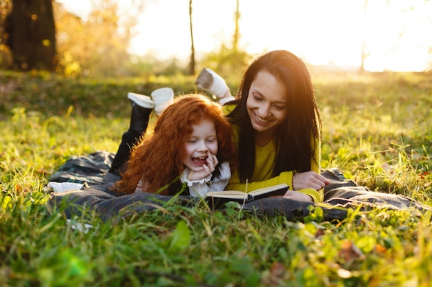 Ambiance d&#39;automne, portrait de famille. Charmante maman et sa fille aux cheveux roux s&#39;amusent assises sur le tombé