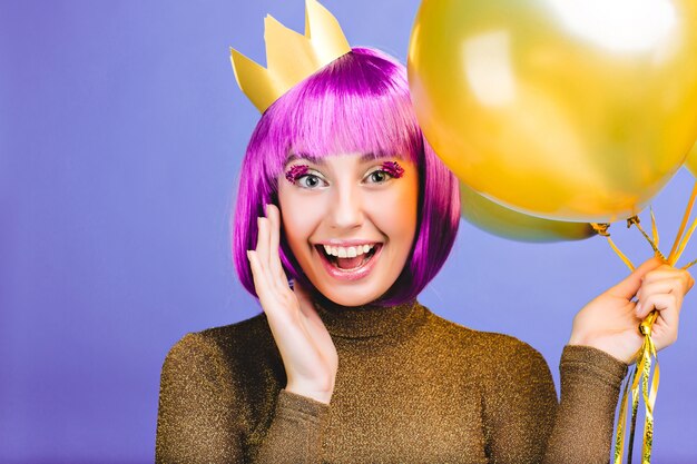 Ambiance de fête du nouvel an de la belle jeune femme drôle avec des ballons dorés. Couper les cheveux violets, la couronne, la robe de luxe, les émotions vives, exprimer la positivité, la célébration.